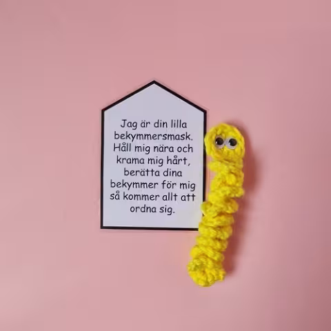 En liten virkad mask i gul färg med en lapp fäst vid sig